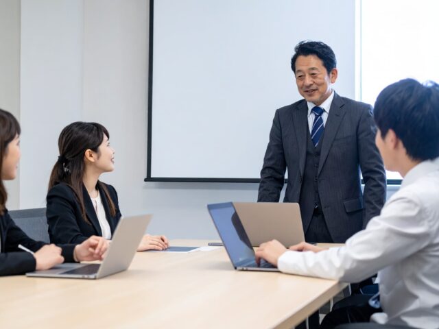 会議室で社長の話を聞く新入社員