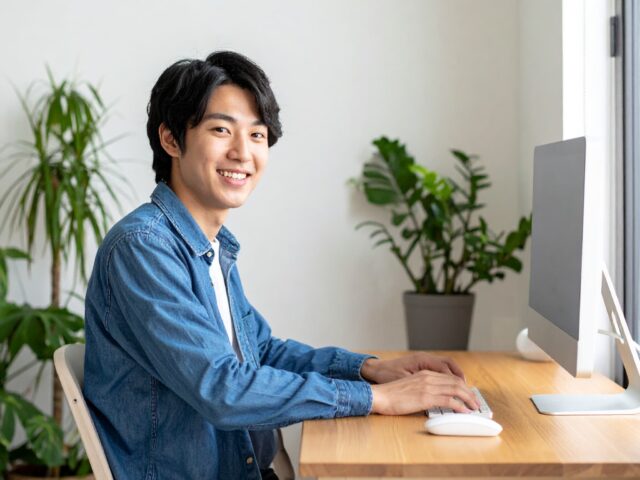 自宅デスクでパソコン作業をする大学生
