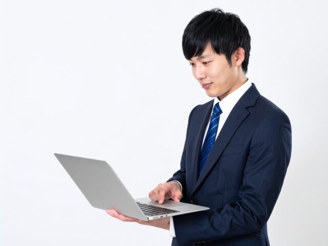 ノートパソコンを手に持ち操作する男性