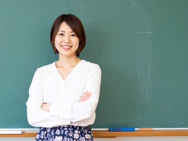 黒板の前で腕を組む女性教師