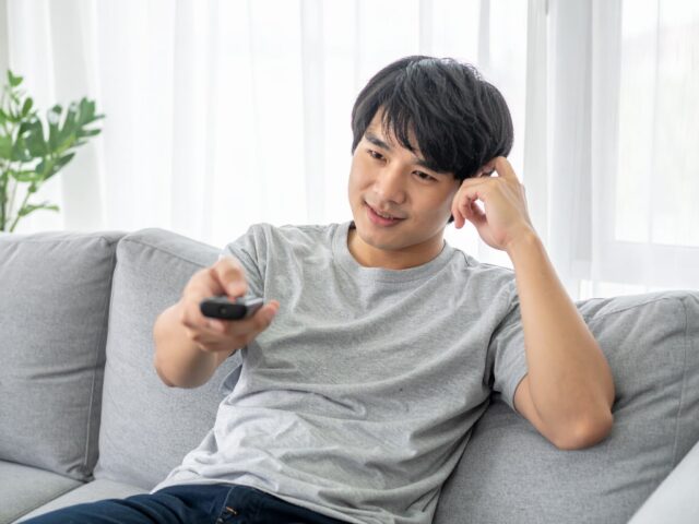ソファに座りリモコンを操作する男性