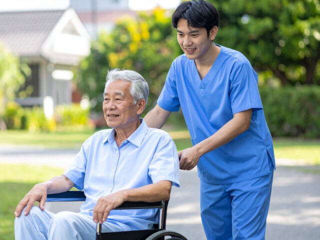 車椅子で散策する高齢男性と介護士
