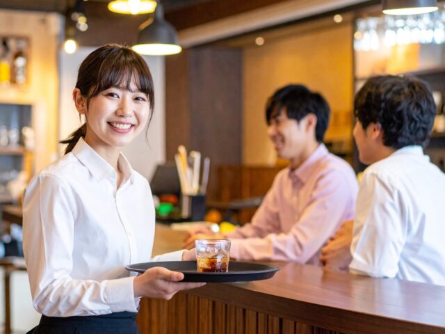 おしゃれなバーのカウンターで笑顔で接客する女性バーテンダー