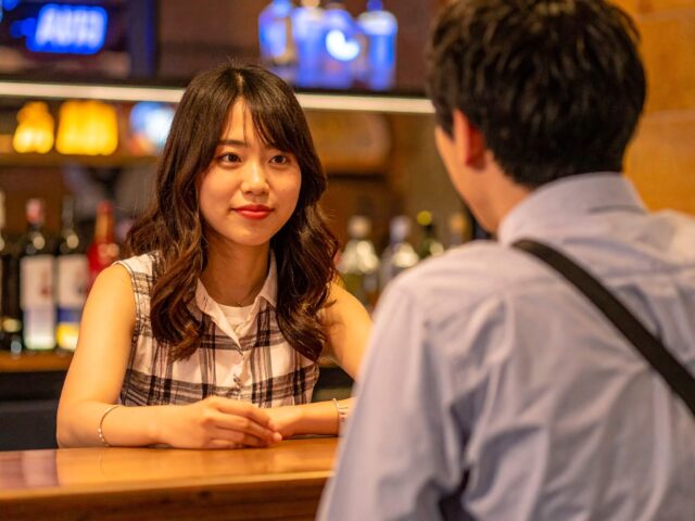夜のバーカウンターで男性客と談笑する若い女性