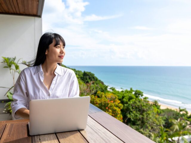 海を眺めながらPC作業をする女性の写真