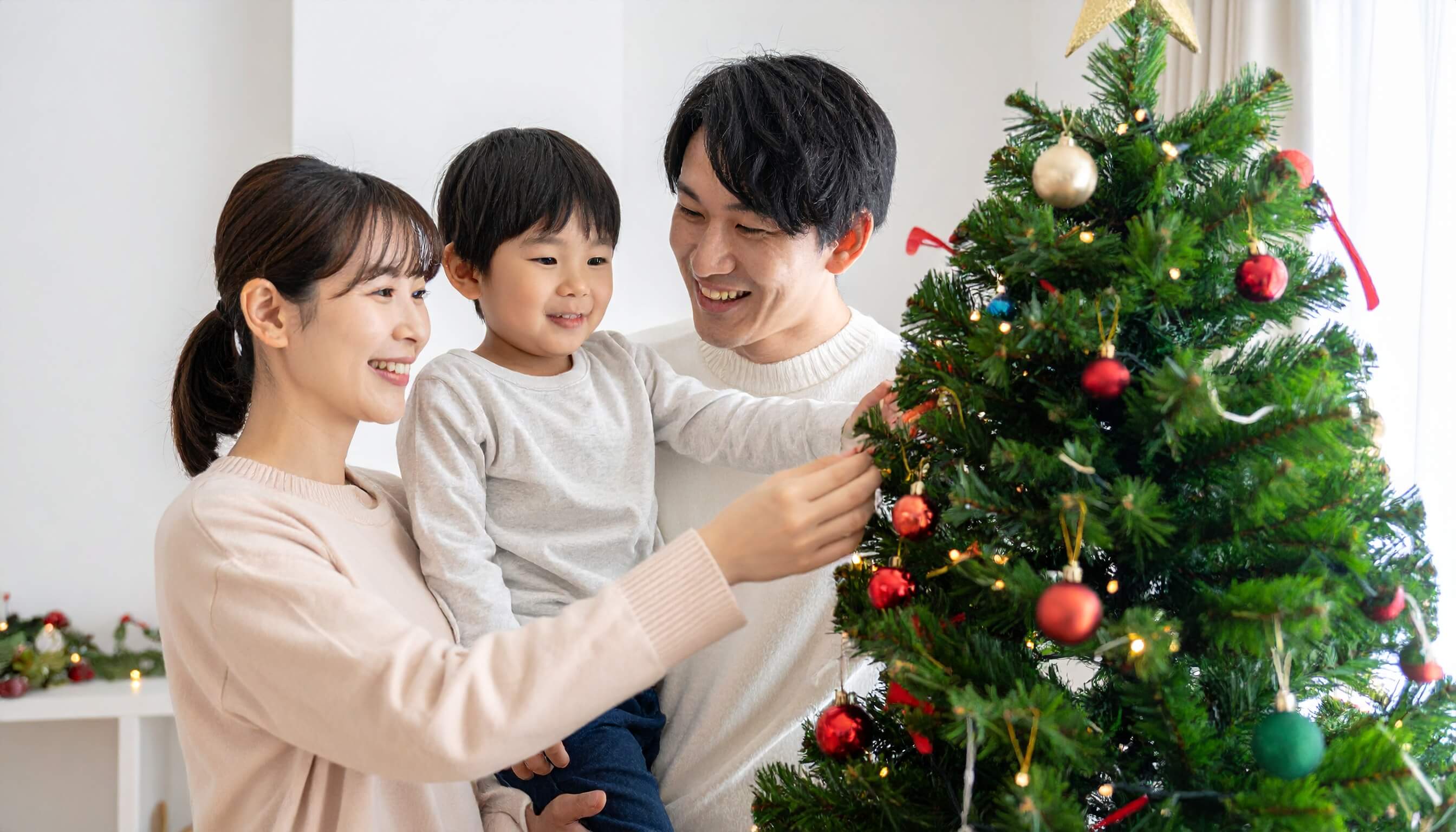 笑顔でクリスマスツリーを飾る若い夫婦と子供