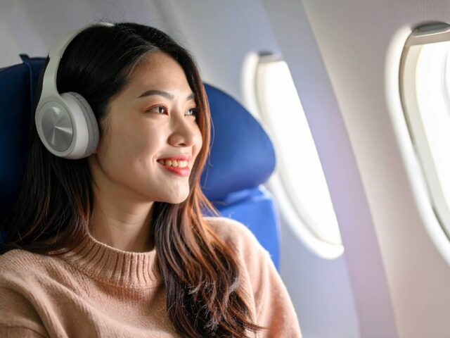 飛行機の窓際でヘッドホンをして音楽を聴く笑顔の女性