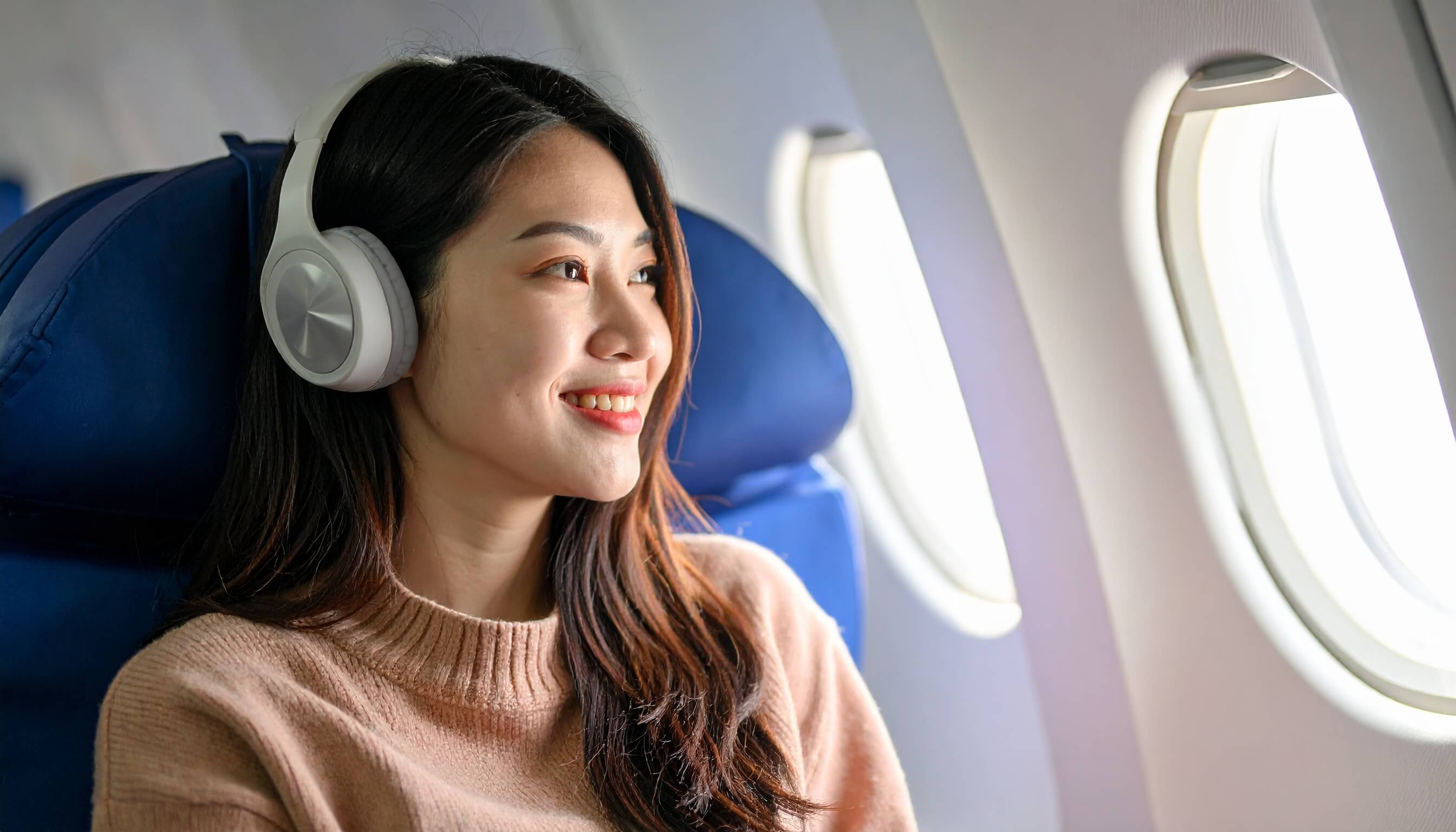 飛行機の窓際でヘッドホンをして音楽を聴く笑顔の女性