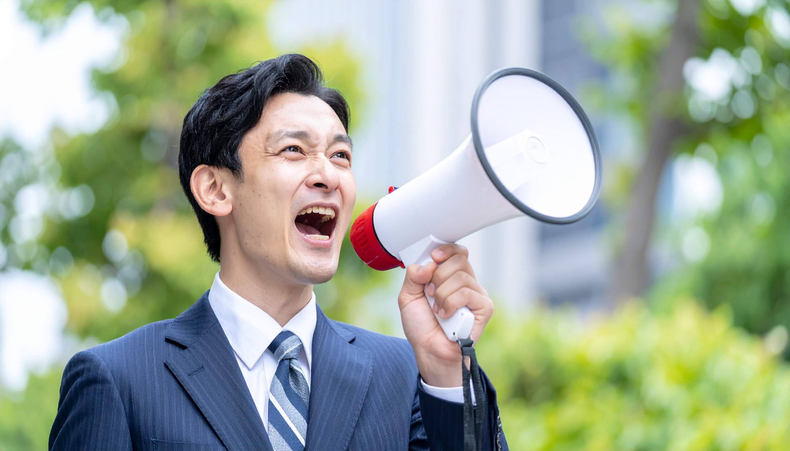 屋外でメガホンを使って大声で叫ぶスーツ姿の日本人男性