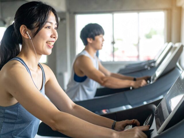 スポーツジムのランニングマシンで笑顔で汗を流す女性