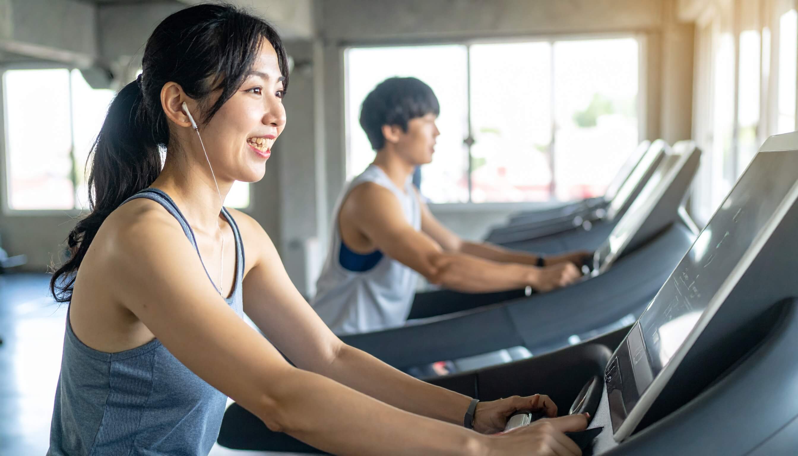 スポーツジムのランニングマシンで笑顔で汗を流す女性