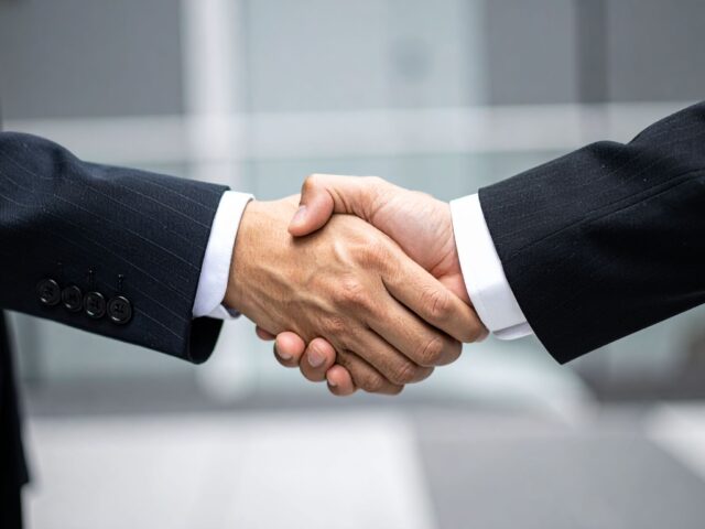 契約成立を祝してがっちりと握手を交わすビジネスマンの手元