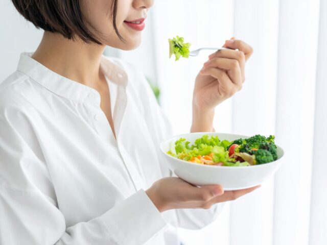 窓際で新鮮な野菜サラダを食べる笑顔の日本人女性
