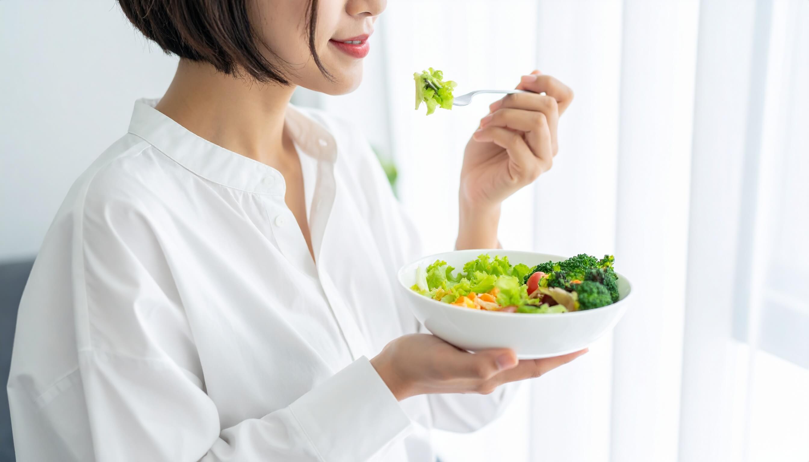 窓際で新鮮な野菜サラダを食べる笑顔の日本人女性